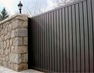 Muro de piedra junto a una alta puerta de metal oscuro a lo largo de un sendero pavimentado.