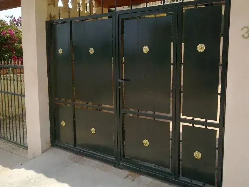 Puerta metálica cerrada de color verde oscuro con detalles dorados en la entrada de una casa.