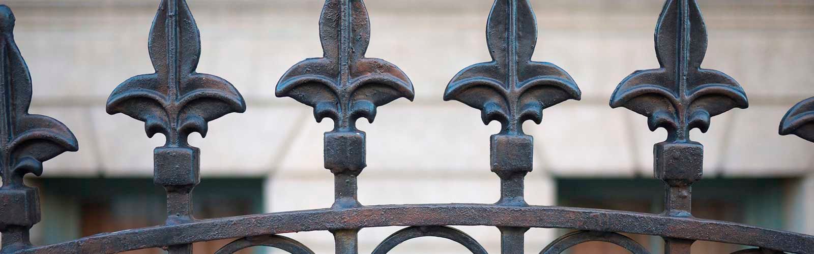 Valla de hierro forjado negro con remates en forma de flor de lis contra la pared de un edificio de piedra.