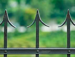 Valla de hierro negro con remates puntiagudos sobre un fondo verde difuminado.