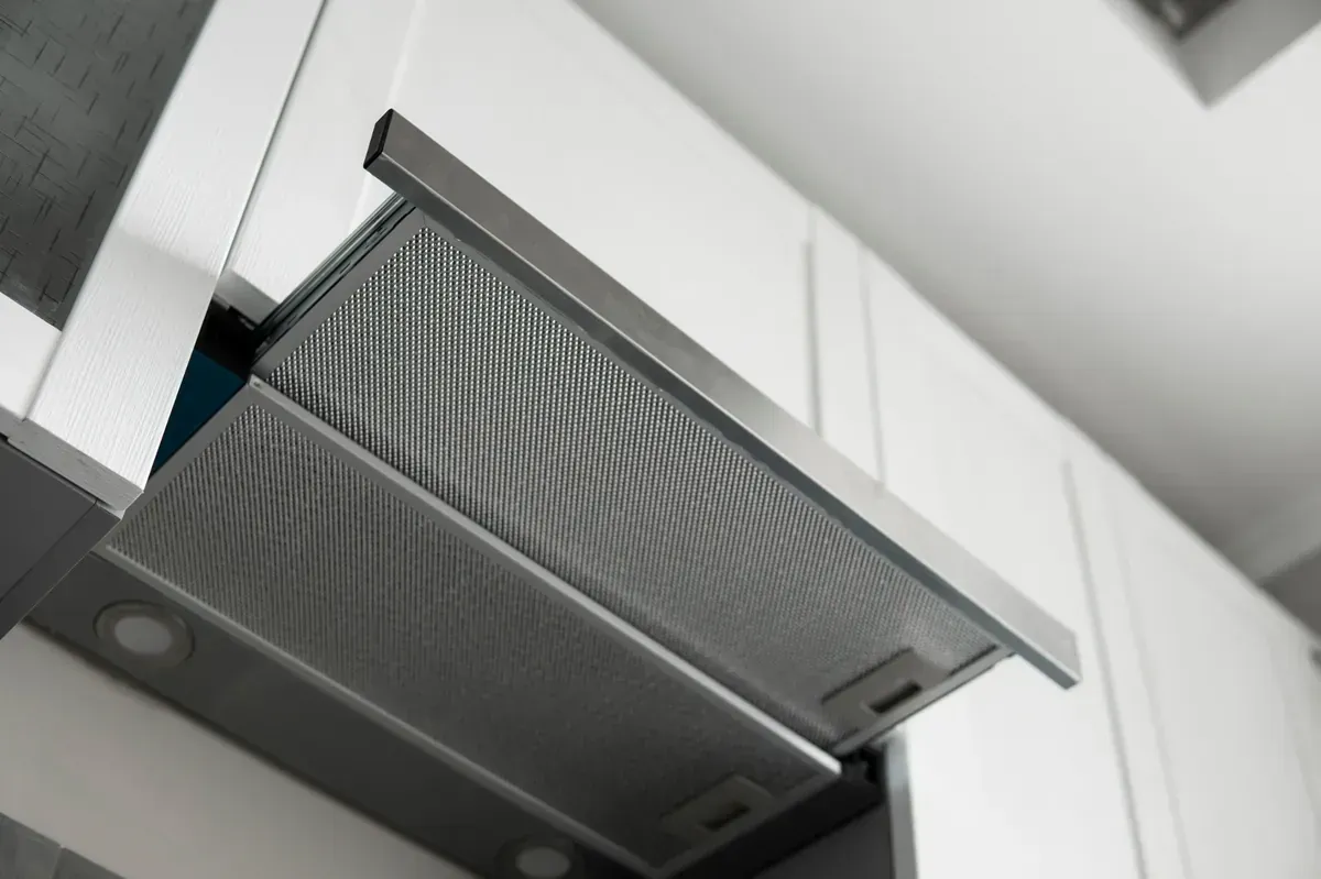 Primer plano de una campana extractora de acero inoxidable con filtro en una cocina blanca.