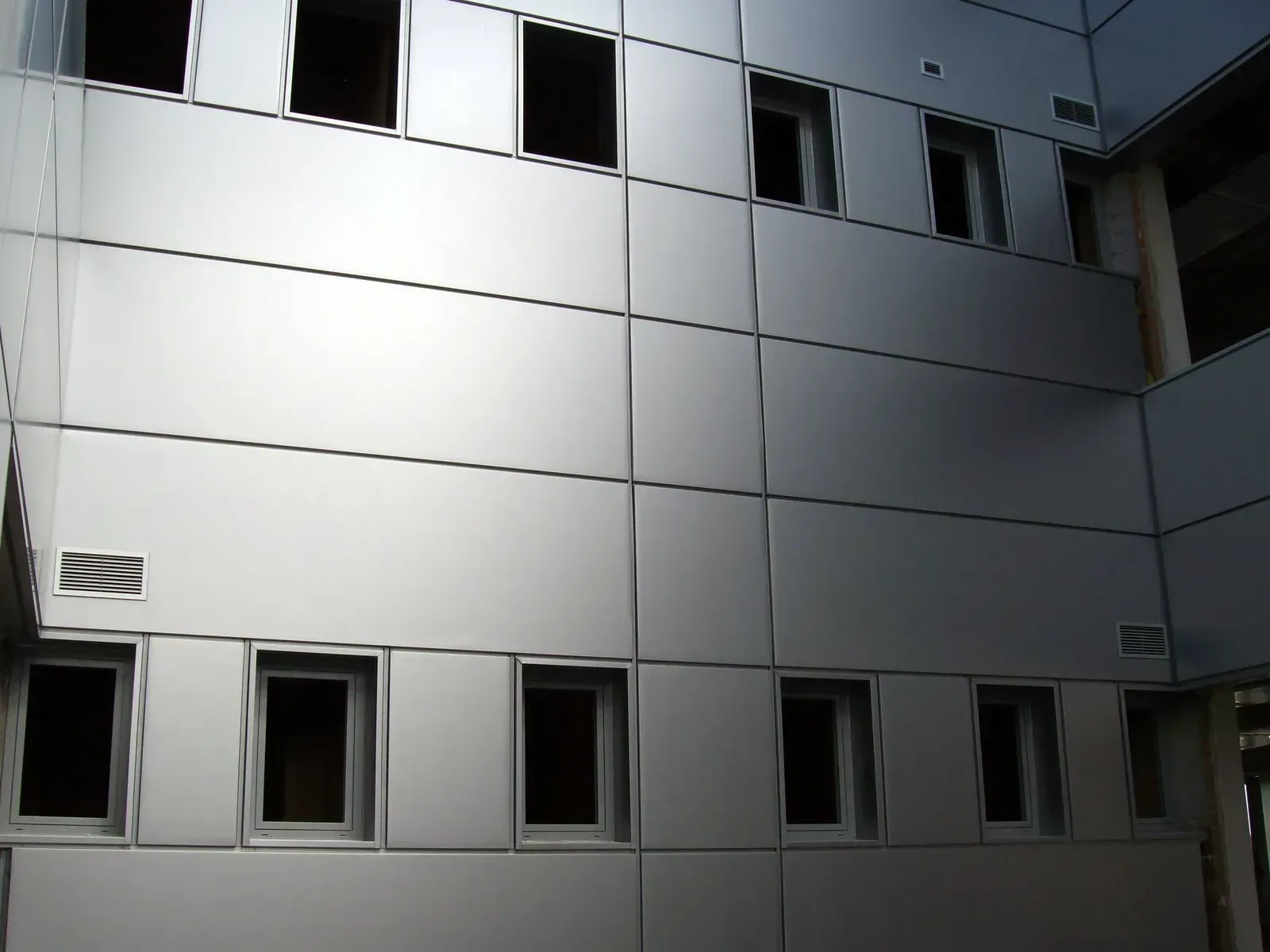Un edificio moderno con fachada revestida de metal plateado y dos filas de ventanas rectangulares.
