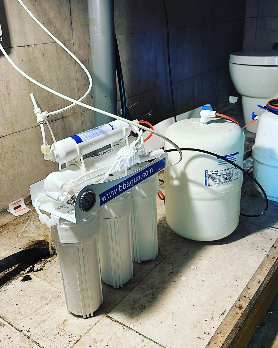 Un filtro de agua está sobre un piso de baldosas al lado de un inodoro.
