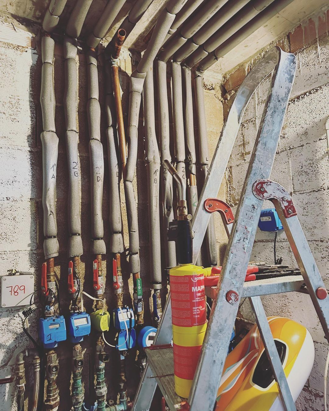 Una escalera está colocada delante de una pared de tuberías.