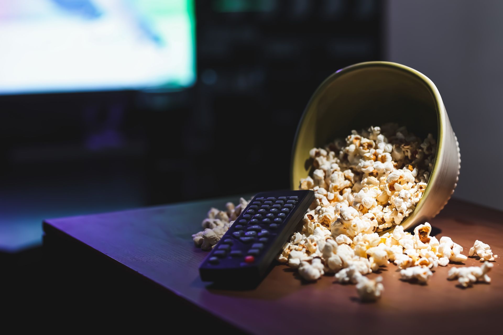 Bol de popcorn renversé sur une table avec une télécommande, ambiance cinéma à domicile