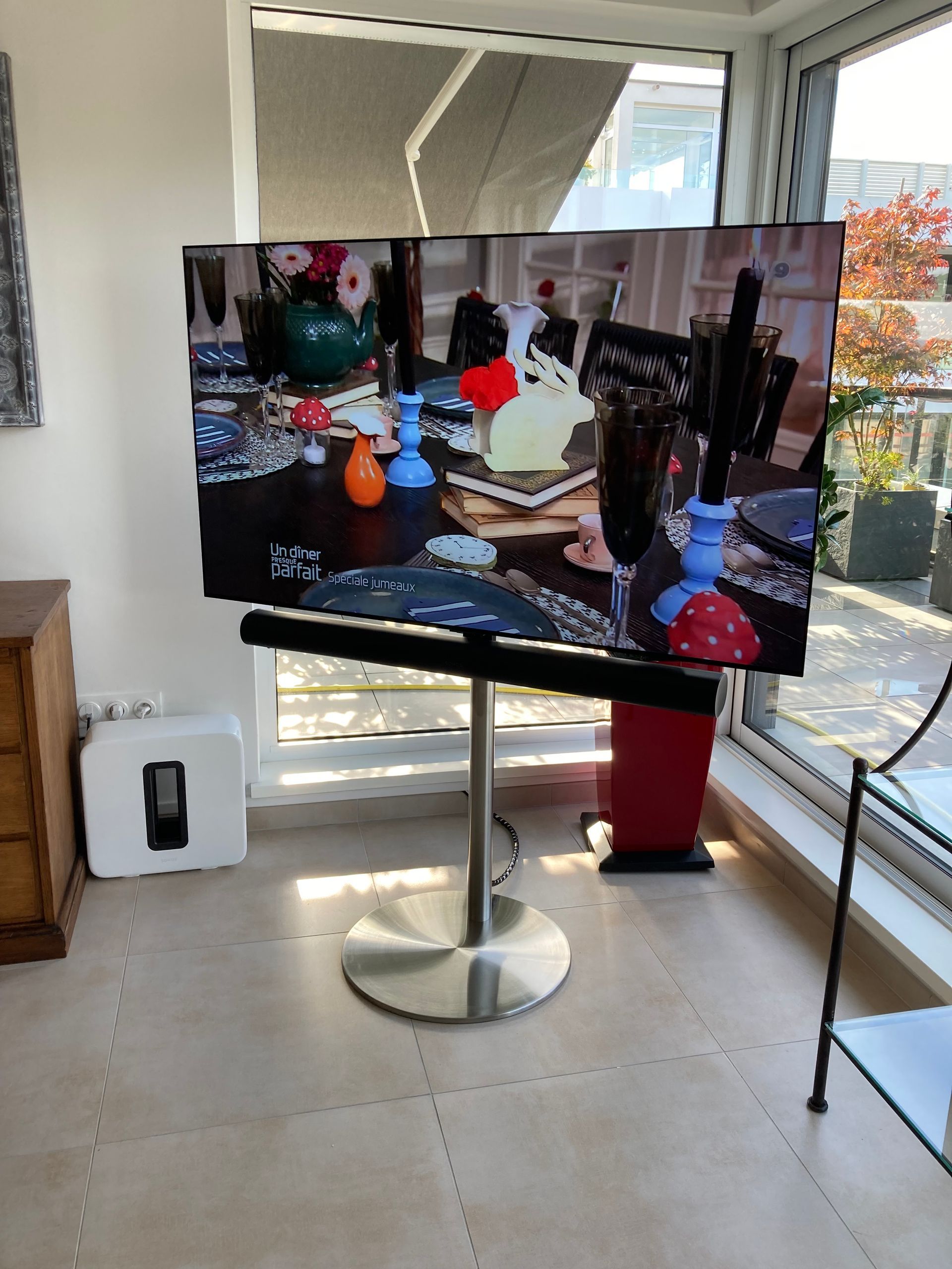 Télévision sur un pied en inox installée devant une baie vitrée