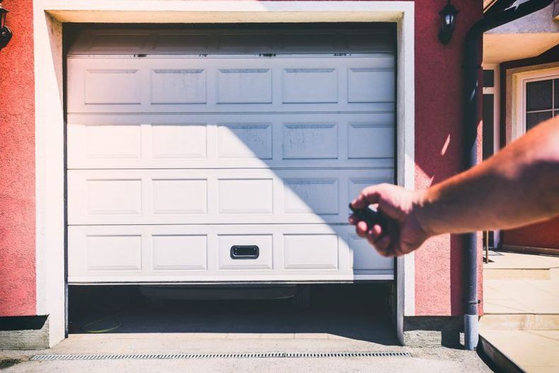 Main tenant une télécommande de porte de garage à côté d'une porte de garage blanche en plein jour