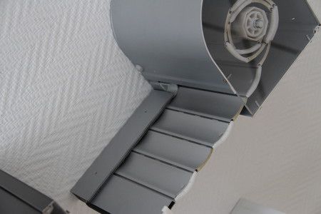Gros plan sur un escalier en colimaçon en métal gris devant un mur blanc.
