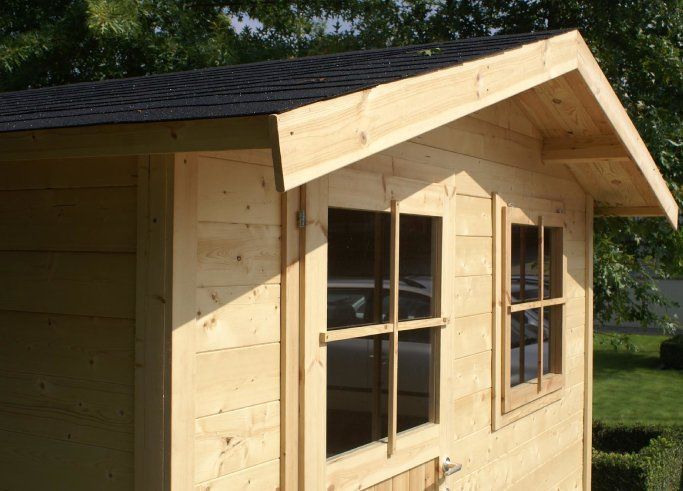 Abri de jardin en bois avec un toit foncé et des fenêtres en façade, dans une cour gazonnée.