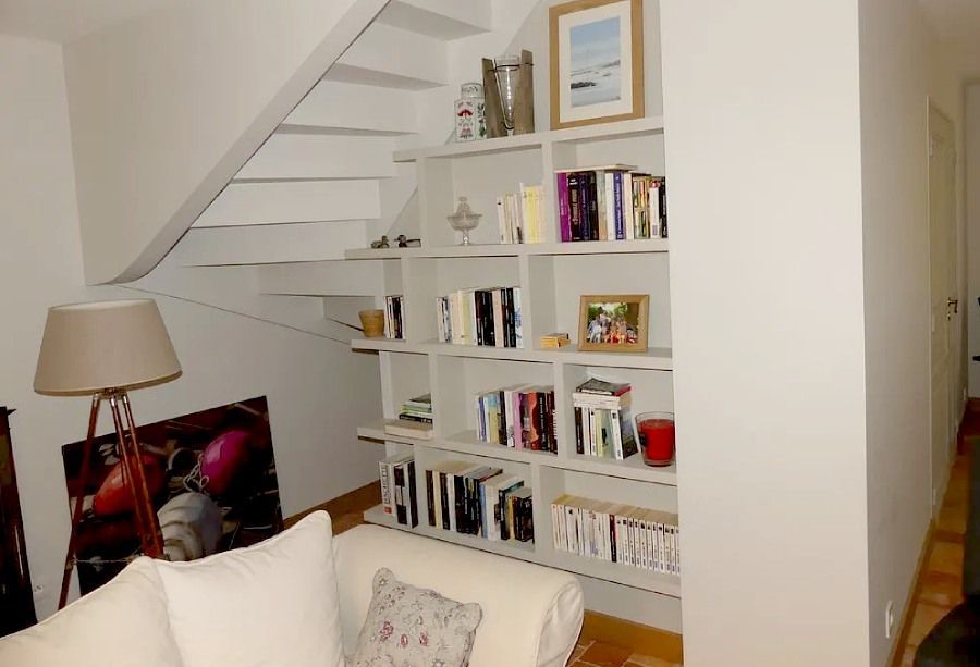 Salon avec escalier blanc, bibliothèque intégrée, lampe et coussins de canapé.