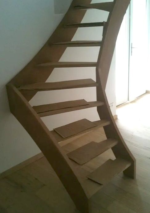 Un escalier en bois incurvé aux marches ouvertes jouxte une porte lumineuse dans un intérieur épuré.