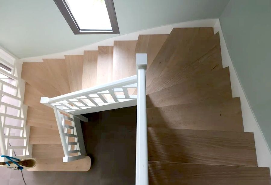 Vue de dessus d'un escalier en bois incurvé avec une rampe blanche et une lucarne au-dessus.