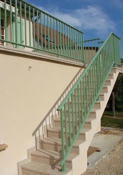 Escalier extérieur en béton avec rampes en métal vert, à côté d'un bâtiment beige.