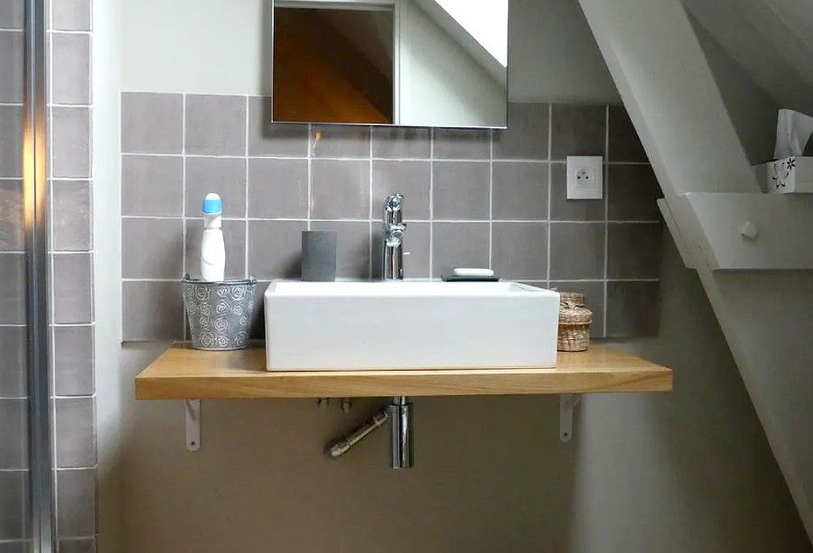 Lavabo de salle de bains avec comptoir en bois, mur carrelé gris, miroir, robinet et articles de toilette.