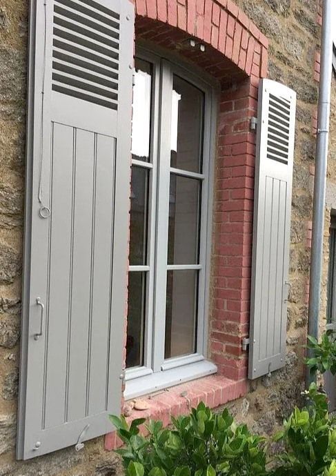 Fenêtre d'une maison en pierre avec des volets gris et un parterre de fleurs en dessous