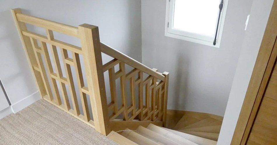 Escalier avec rampe en bois clair à côté d'un couloir recouvert de moquette et d'une fenêtre