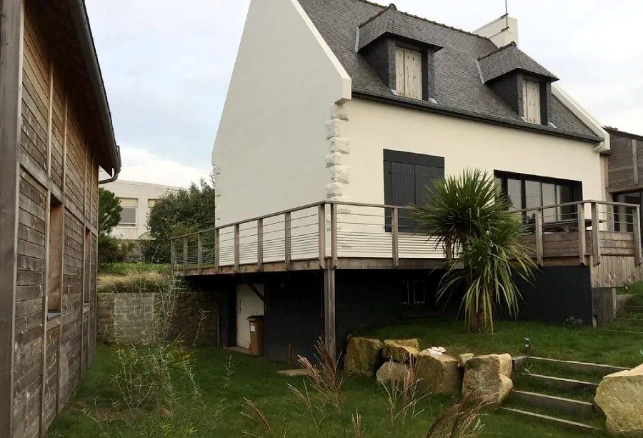 Maison blanche moderne avec toit foncé, terrasse en bois surélevée et jardin gazonné avec escalier en pierre