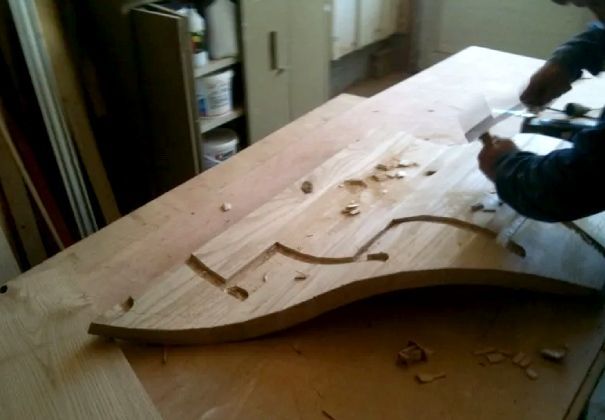 Corps de guitare en bois en cours de fabrication sur un établi, avec des outils et des copeaux de bois à proximité