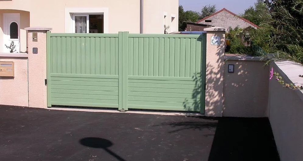 Portail double vert donnant sur une maison couleur pêche avec une allée pavée à l'avant.