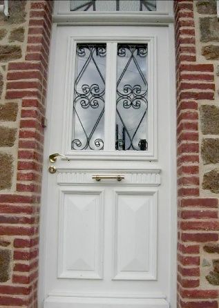 Porte d'entrée blanche avec panneaux de verre décoratifs en fer forgé, encastrée dans un mur de briques rouges.