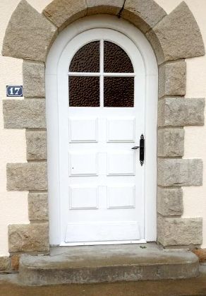 Porte à panneaux blancs avec cadre en pierre arqué et le numéro 17 au-dessus d'une marche.