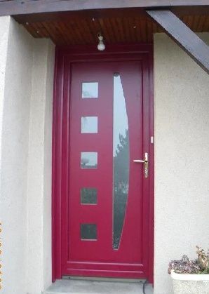 Porte d'entrée rouge avec fenêtres carrées et longue baie vitrée étroite sous un porche