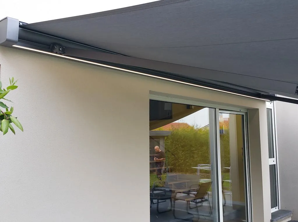 Extérieur de maison moderne avec un auvent gris au-dessus d'une porte-fenêtre coulissante et des sièges de patio visibles à l'intérieur