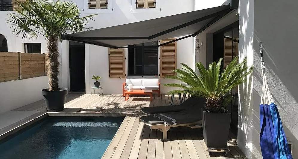 Cour intérieure moderne avec une petite piscine, une chaise longue, des palmiers en pot et une voile d'ombrage noire.
