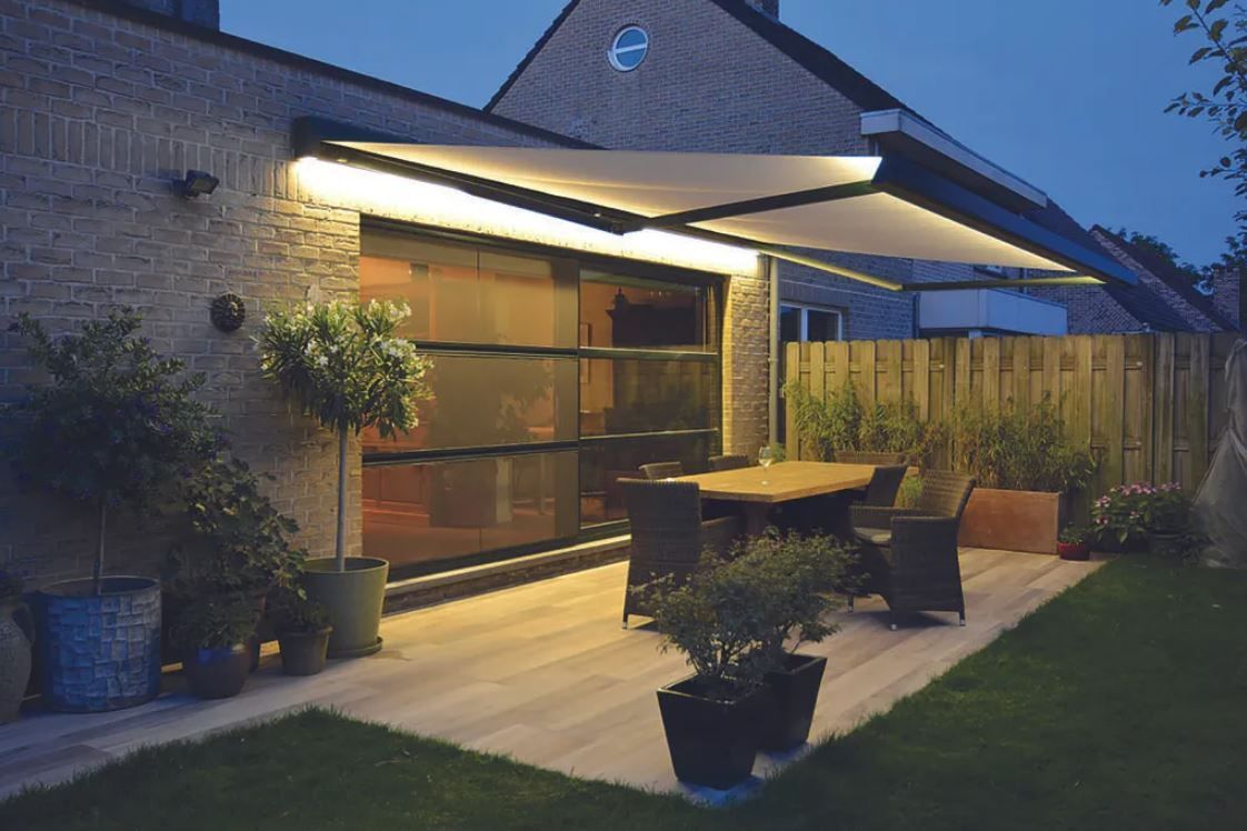 Patio moderne au crépuscule avec table d'extérieur, plantes en pot et toit de patio éclairé à côté d'une maison