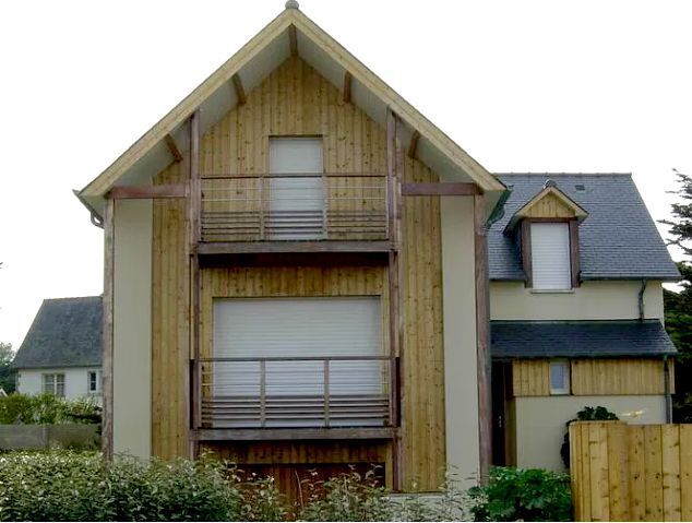 Maison beige à deux étages avec toits à pignons pentus, balcons et clôture en bois à l'avant