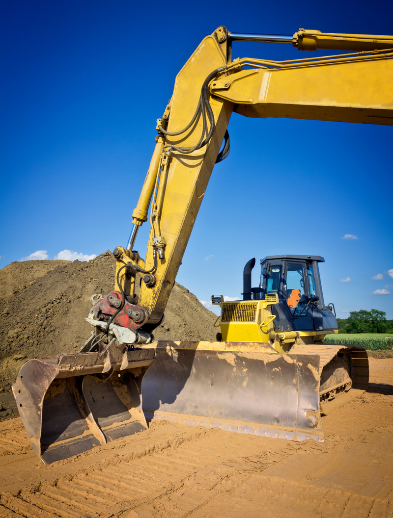 Une excavatrice jaune déplace de la terre sur un chantier de construction.