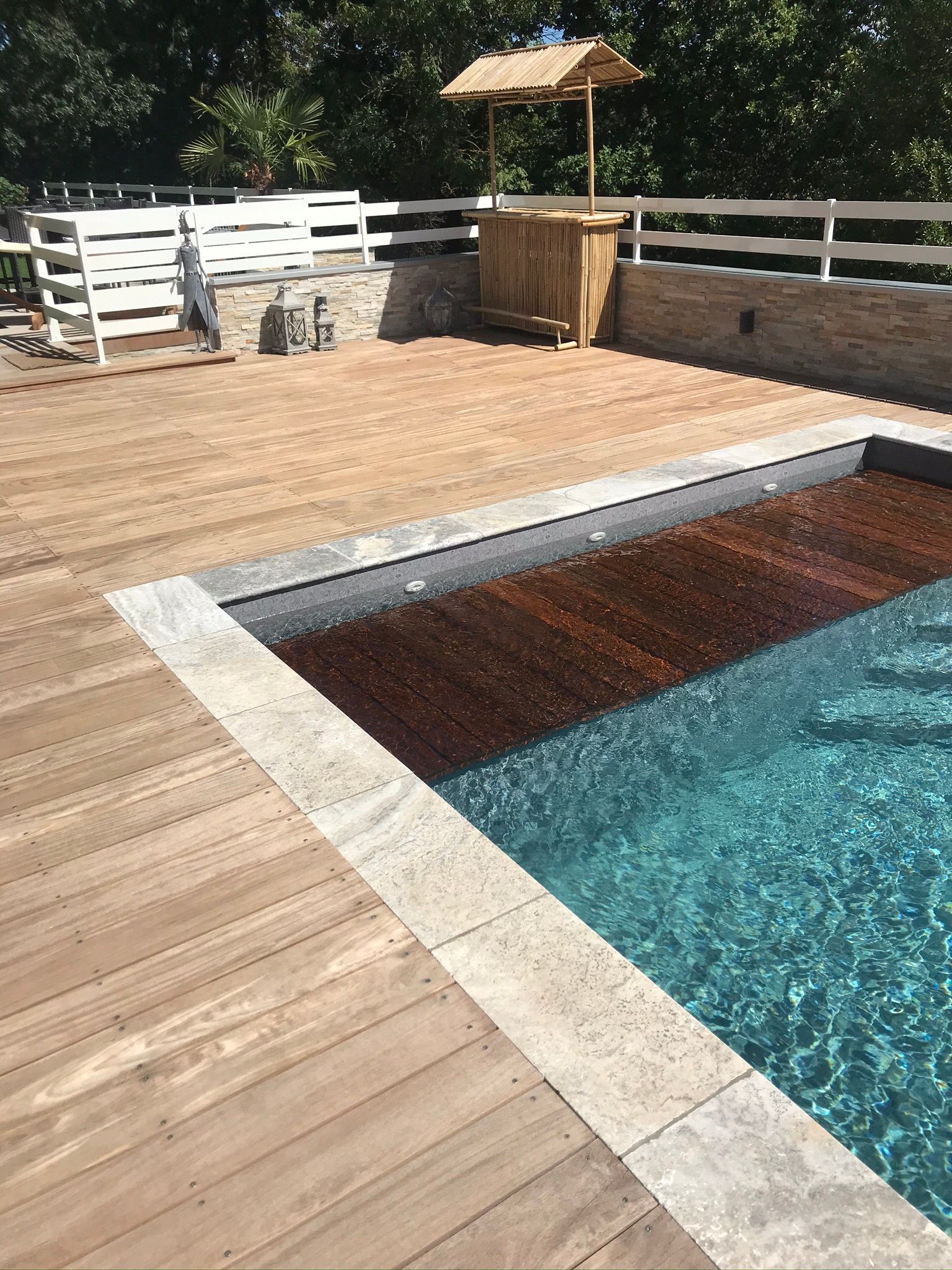 Une piscine avec une terrasse en bois et des margelles en pierre.