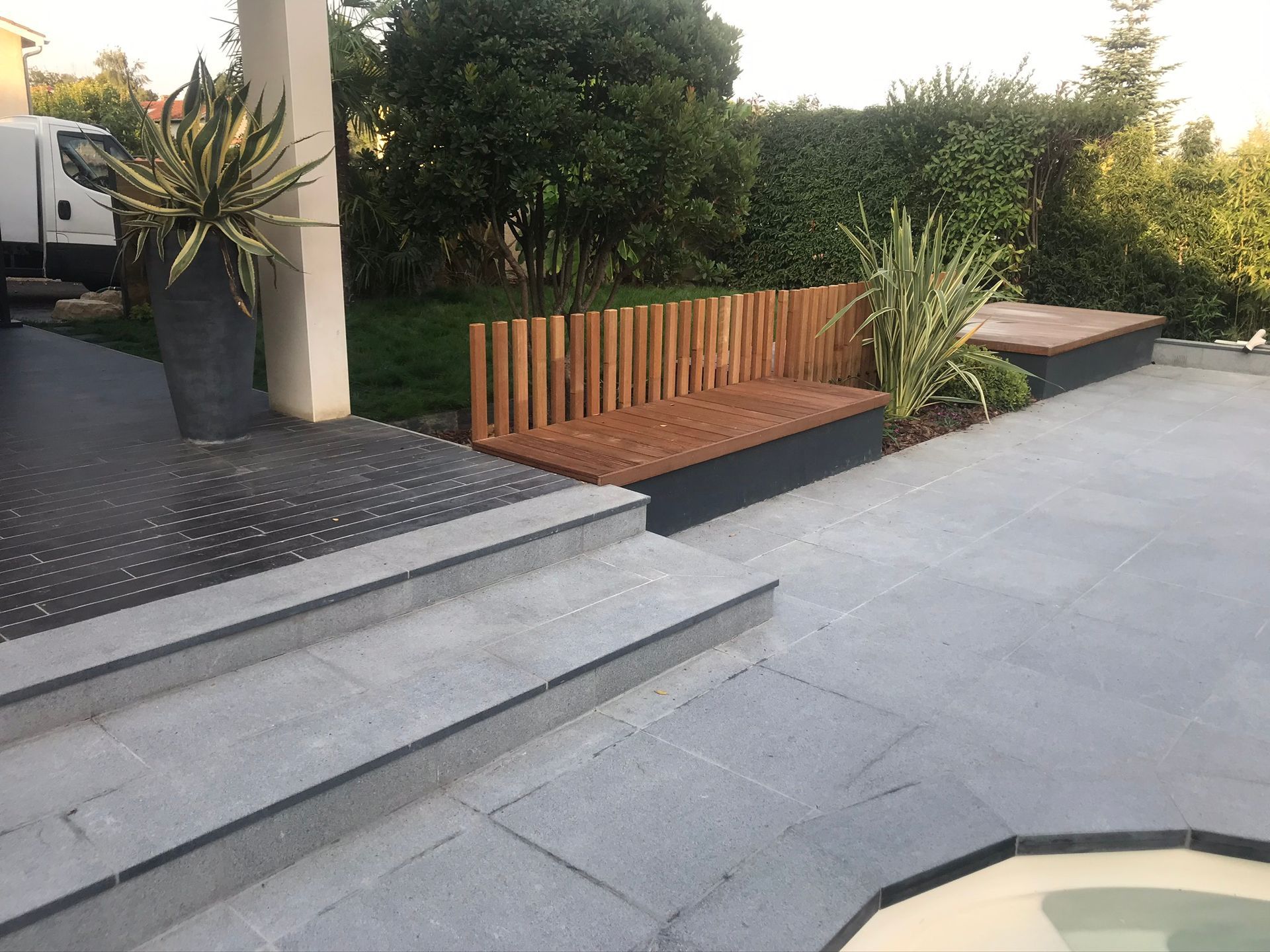 Terrasse carrelée avec un banc et des marches avec des plantations à proximité.