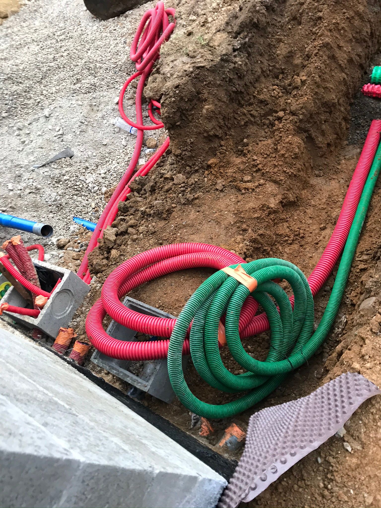 Des câbles électriques rouges et verts enroulés dans une tranchée.