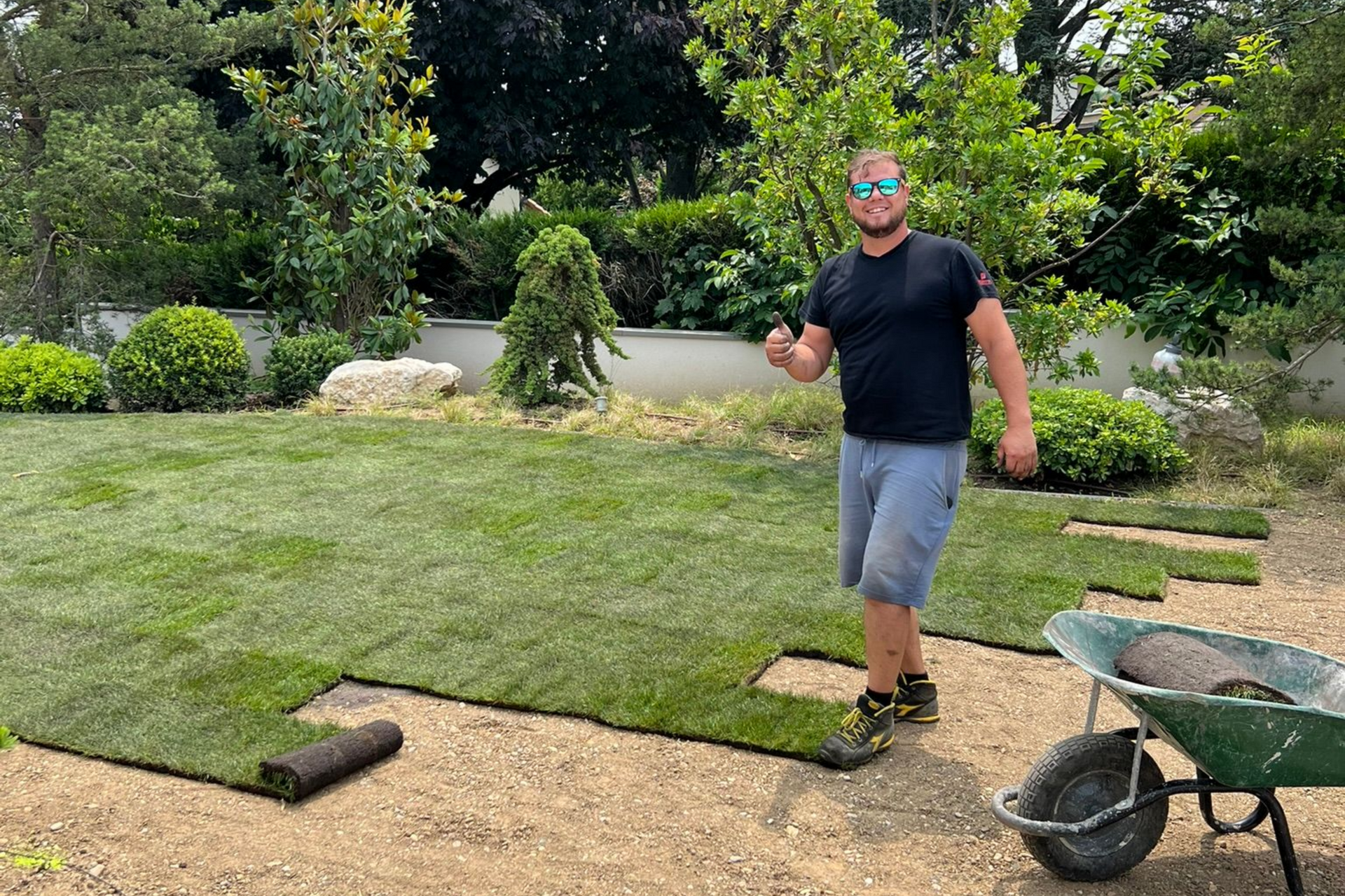 Un homme pose du gazon dans un jardin ensoleillé.