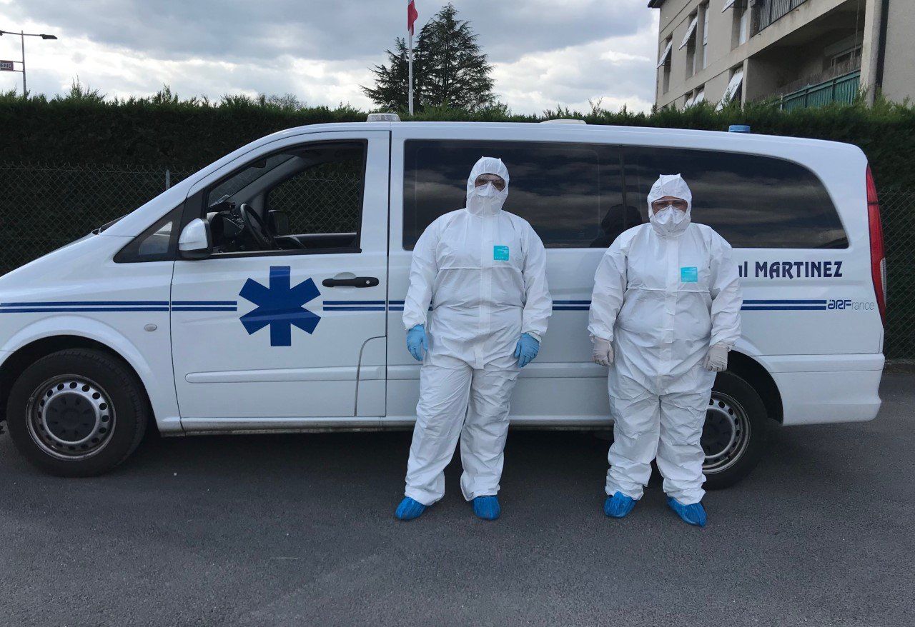 Deux personnes en combinaison intégrale sanitaire devant une ambulance