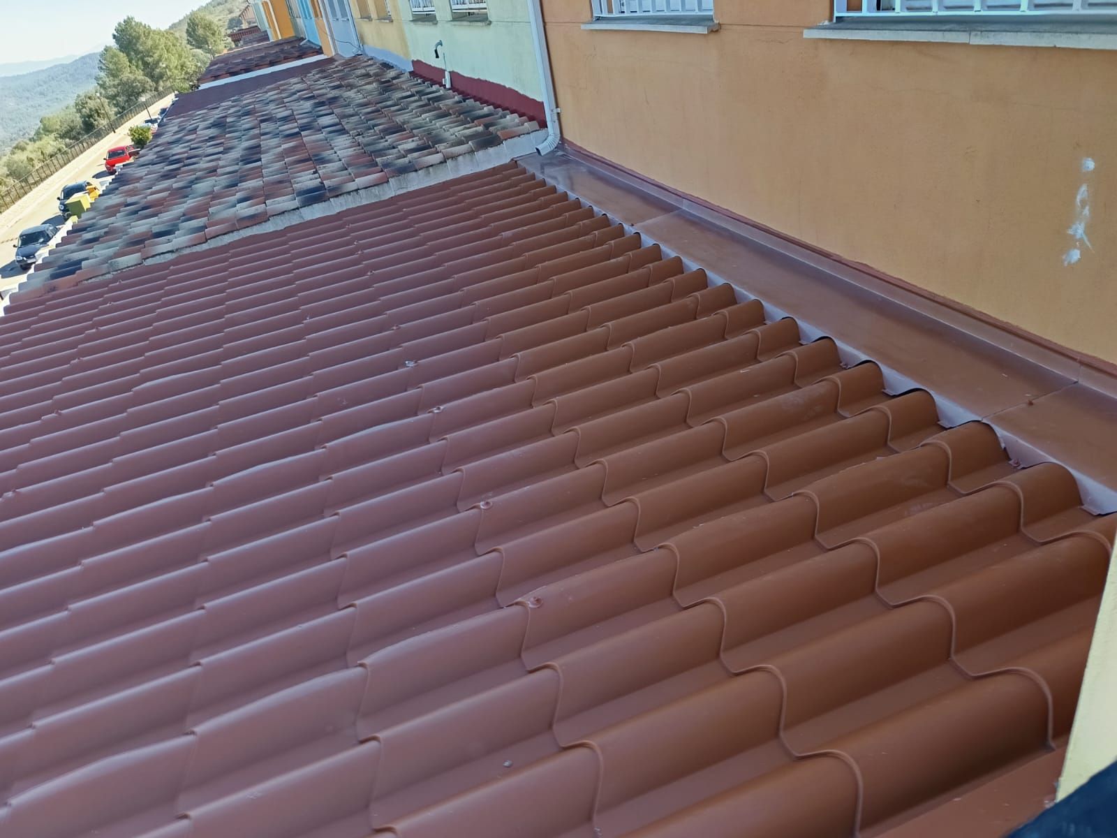Vista desde una ventana que muestra un techo nuevo de tejas rojas junto a un techo