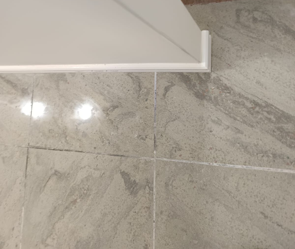 Primer plano de baldosas de suelo de mármol gris claro que se unen a un rodapié blanco y a la esquina de una pared.