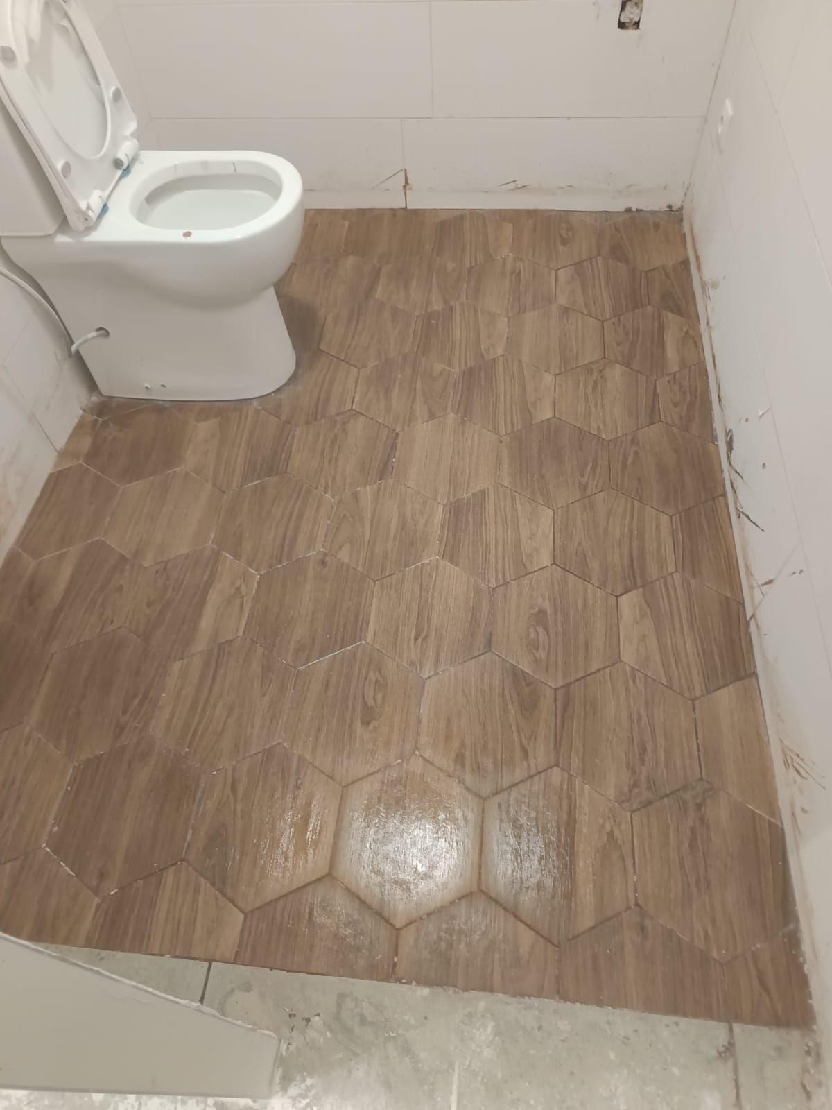 En un baño sin terminar, un inodoro blanco reposa sobre un suelo cubierto