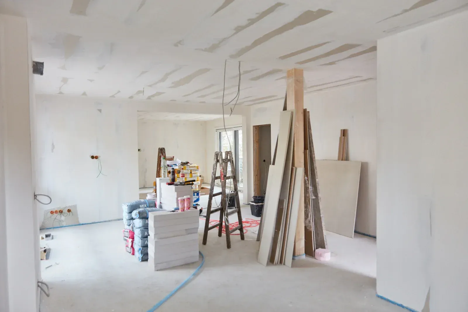 Interior de una habitación en obras con paneles de yeso, una escalera, materiales de construcción y paredes y techo blancos.