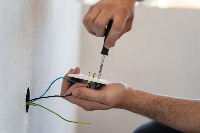 Una persona utiliza un destornillador para cablear un enchufe eléctrico blanco