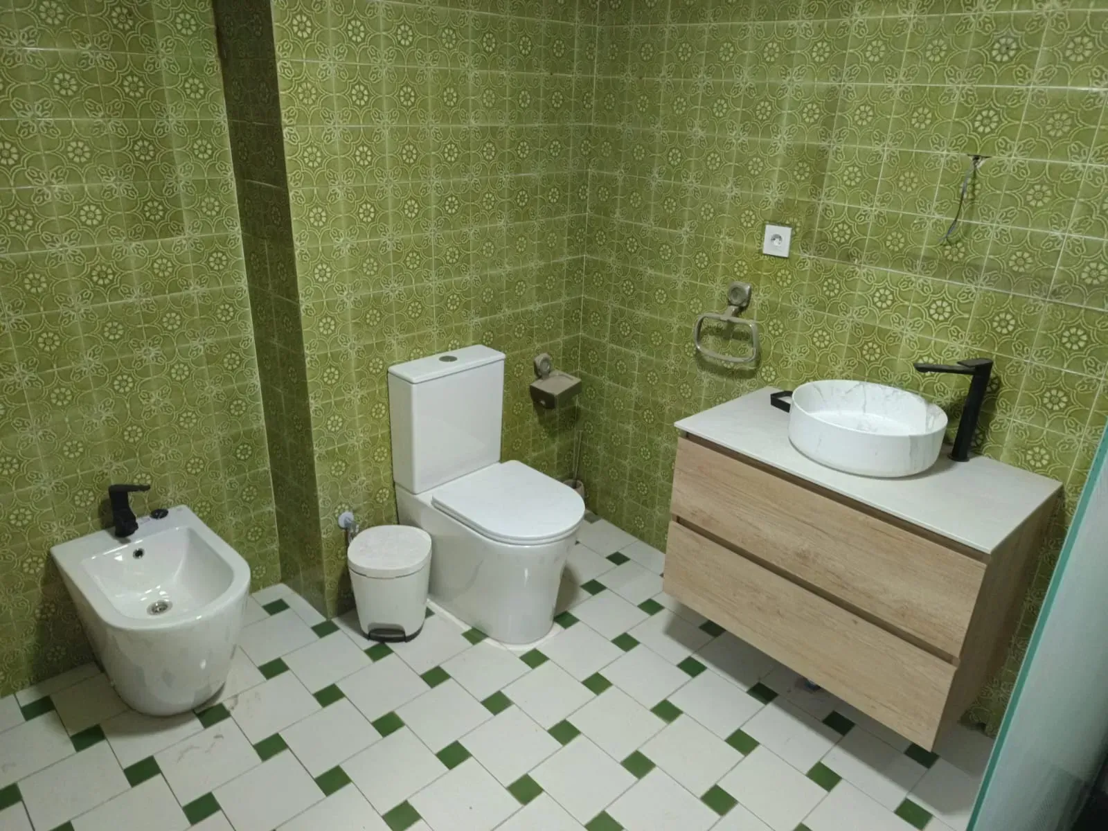 Un baño con azulejos de pared con estampado verde, baldosas blancas