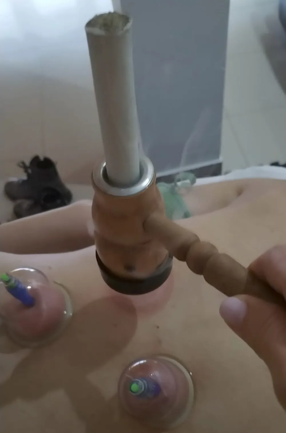 Una mano sostiene un mástil de madera para narguile con dos pequeños recipientes de vidrio sobre una mesa.