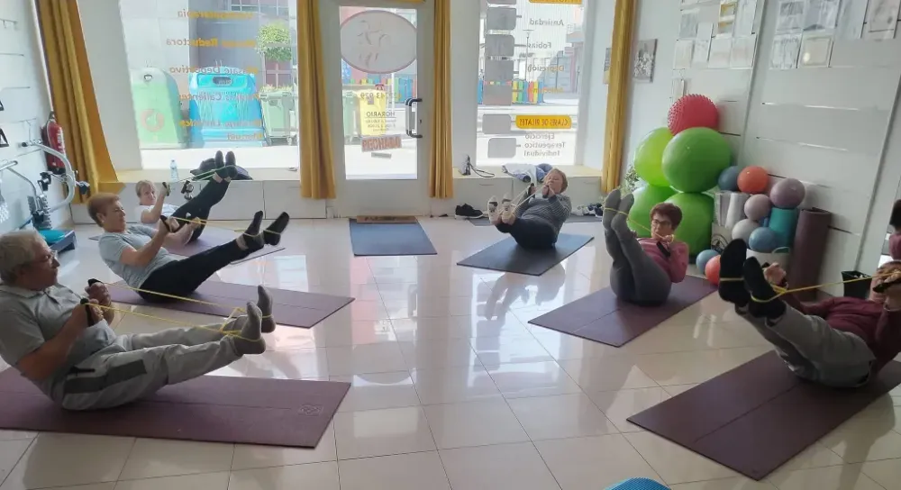 Personas participando en una clase de ejercicios grupales sobre esterillas de yoga en un estudio luminoso.