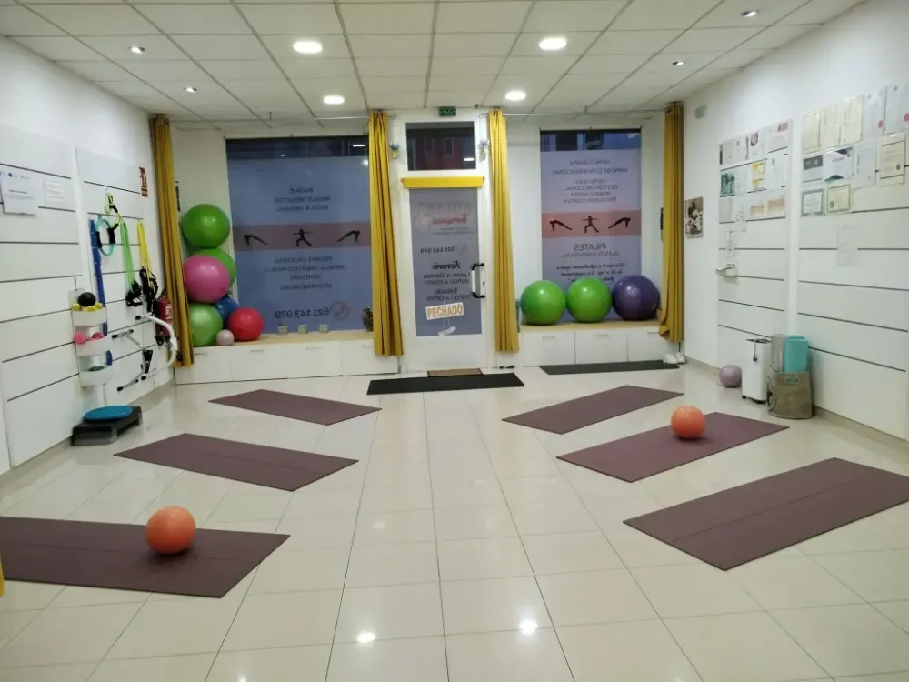Sala de fisioterapia con colchonetas de ejercicio, balones de estabilidad y equipo de rehabilitación sobre suelo de baldosas.
