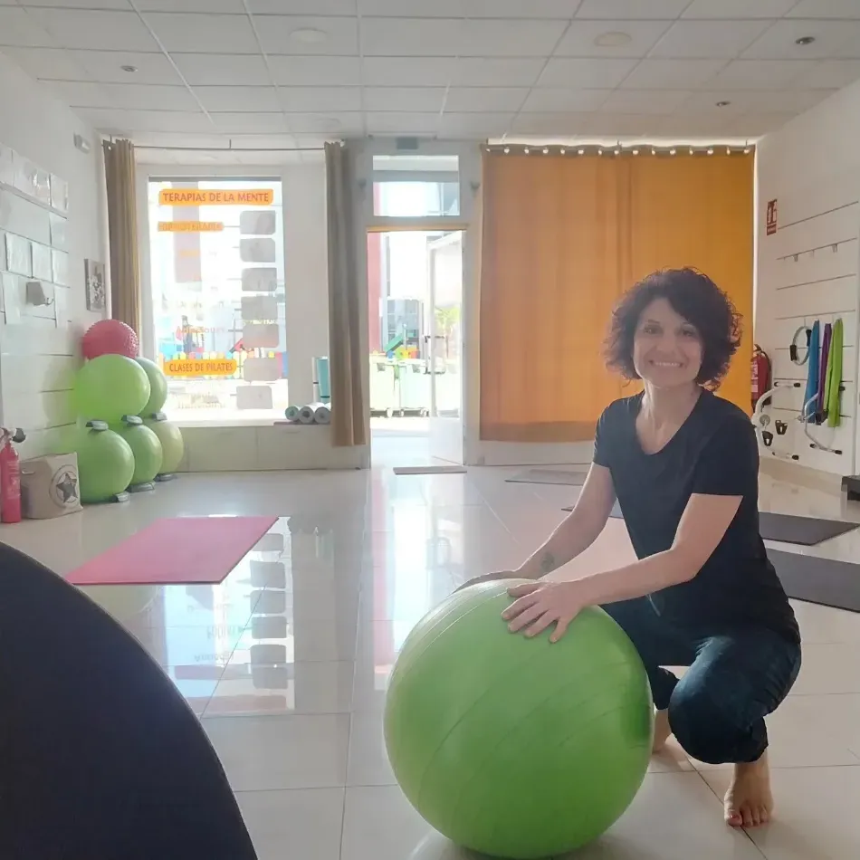 Persona sonriendo mientras está sentada en una pelota de ejercicio verde en un estudio luminoso.