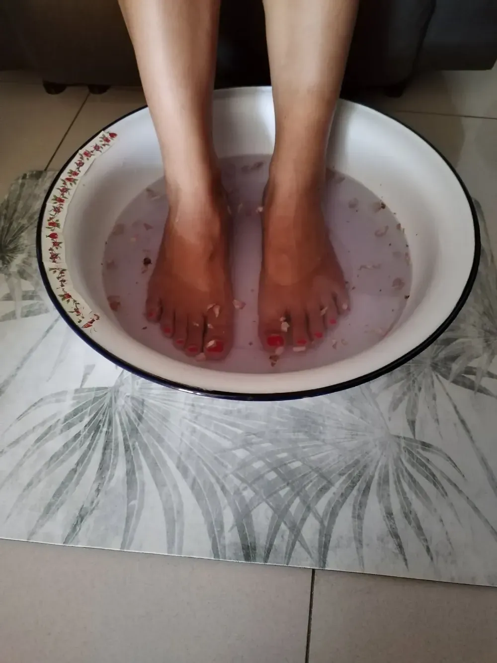 Pies remojándose en una palangana blanca con agua teñida de rosa sobre un suelo de baldosas.