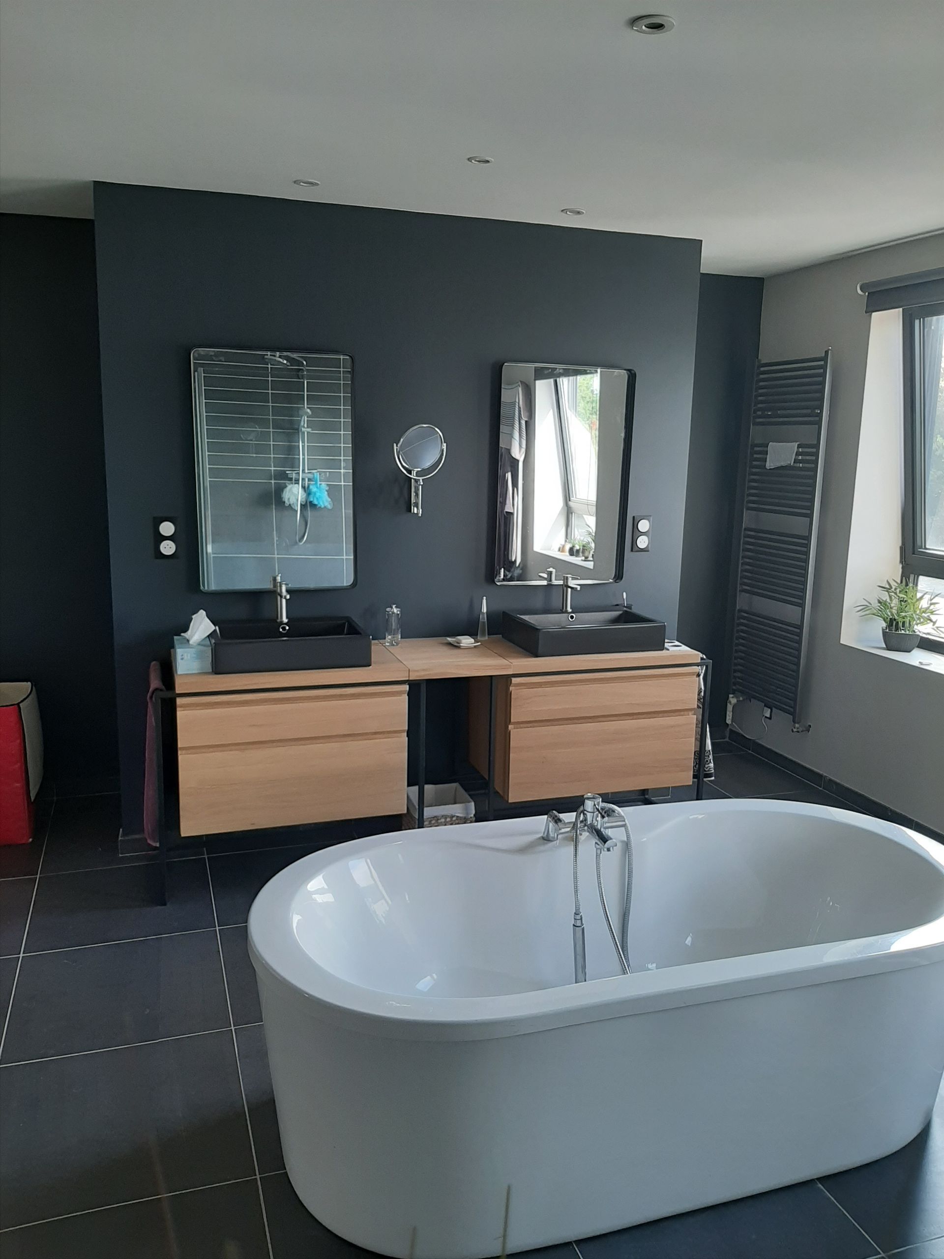 Salle de bain moderne avec baignoire, lavabos noirs et murs gris foncé.
