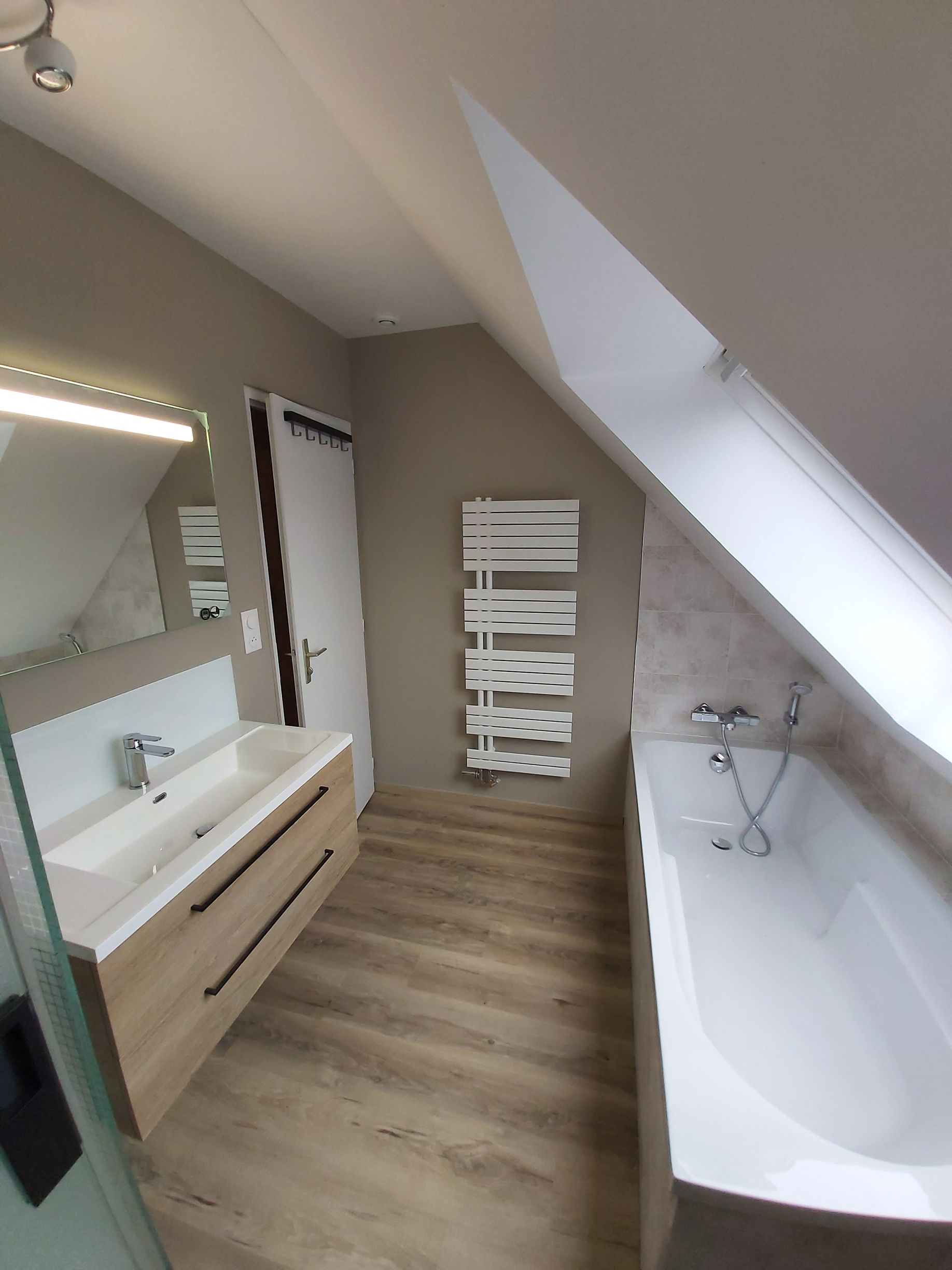 Salle de bain avec plafond en angle, baignoire blanche et porte-serviettes.