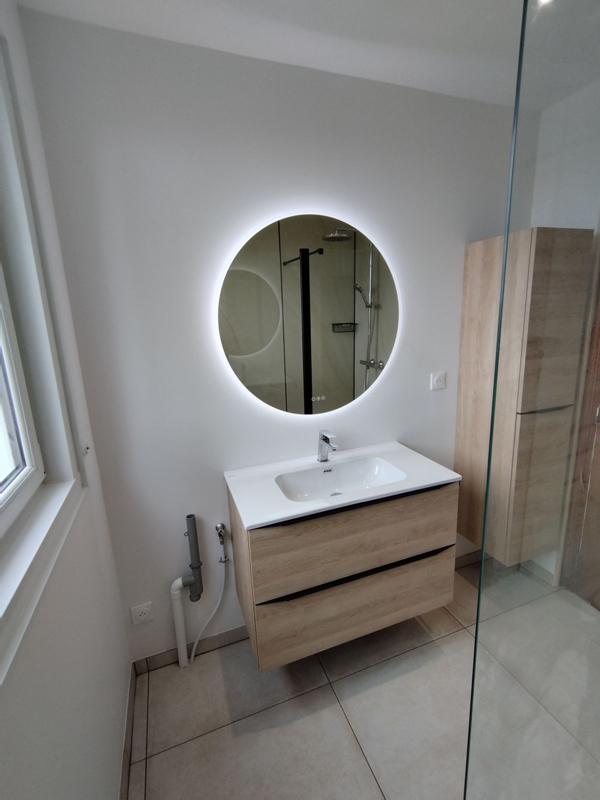 Salle de bain moderne avec un miroir rond et éclairé.